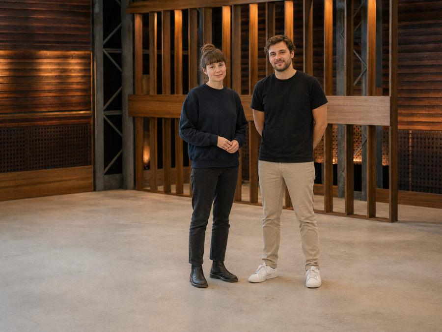 Bildprompt: Fotorealistische Szene — ein junges Gründer-Duo, ein Mann und eine Frau Mitte zwanzig in schlichter dunkler Kleidung, steht selbstbewusst nebeneinander auf einer dezent beleuchteten Pitch-Bühne einer TV-Gründer-Show, vor ihnen unscharf die Silhouetten mehrerer Investoren, auf einem kleinen Podest der weisse NasoZen-Stick (beigefügtes Produktbild als Referenz). Kinoreifes Bühnenlicht, dokumentarisch, hochauflösend.